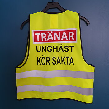 Reflexväst gul. Text vit i röd platta TRÄNAR, svart text UNGHÄST KÖR SAKTA