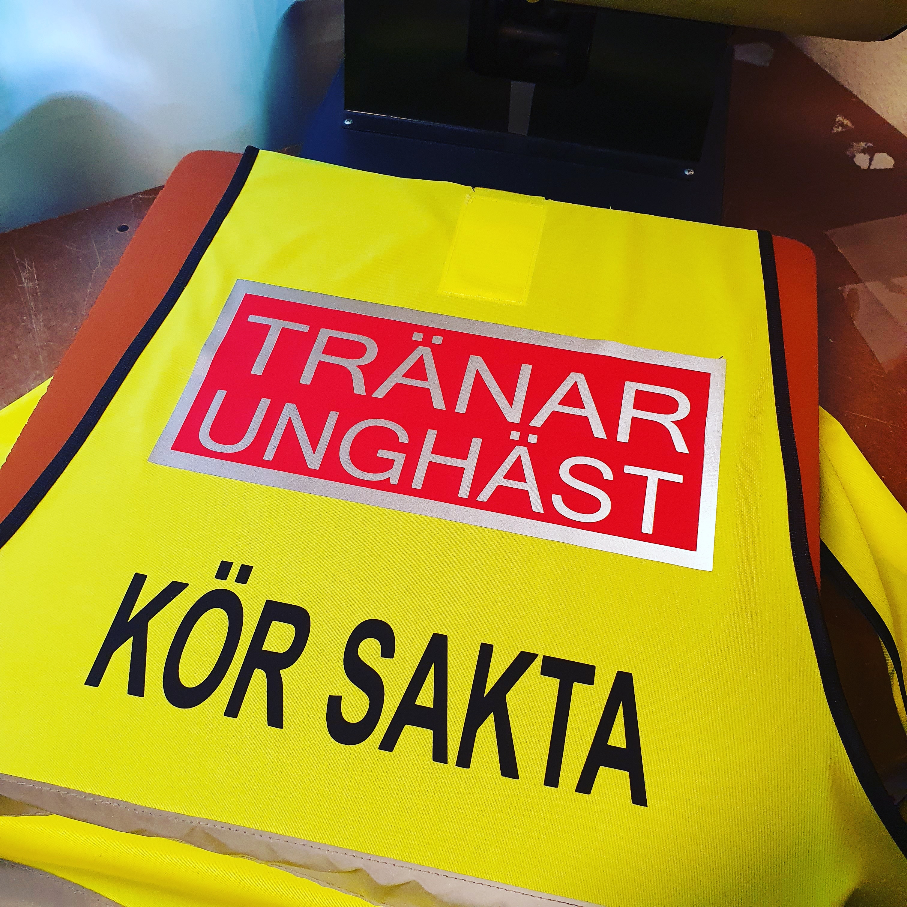 Reflexväst färg gul, Text bak på västen TRÄNAR UNGHÄST i ljusgrå reflex i en rödplatta med reflexram runt. svart text under KÖR SAKTA text fram UNGHÄST RÄDD . - 4