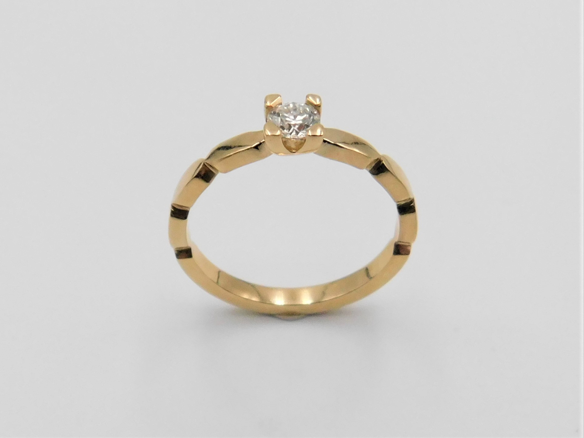 Ring Frida i 18K guld med vågform och briljantslipad diamant i centrum, stående mot ljus bakgrund