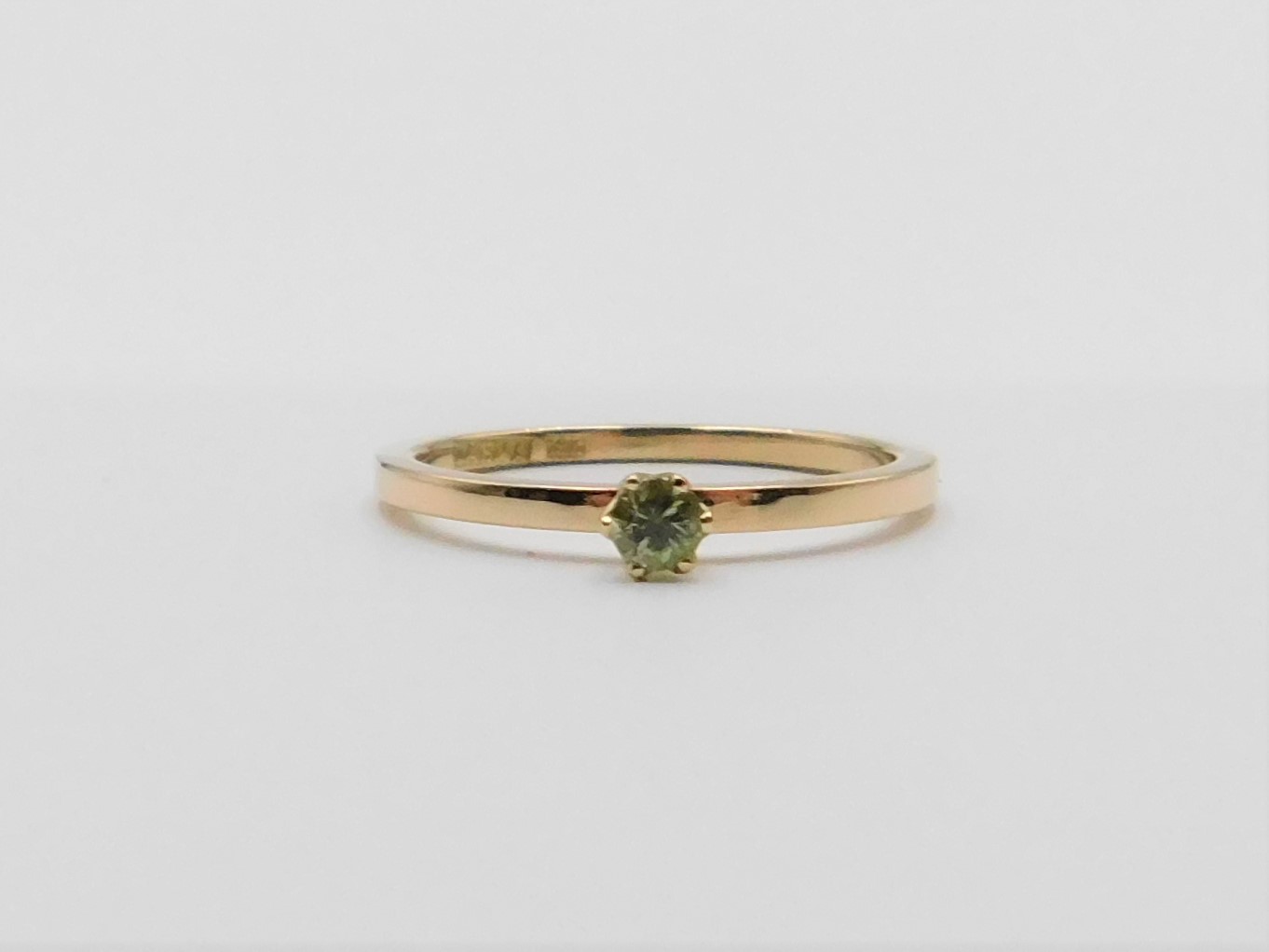 Ring Elly i 18K guld med grön safir liggande mot ljus bakgrund