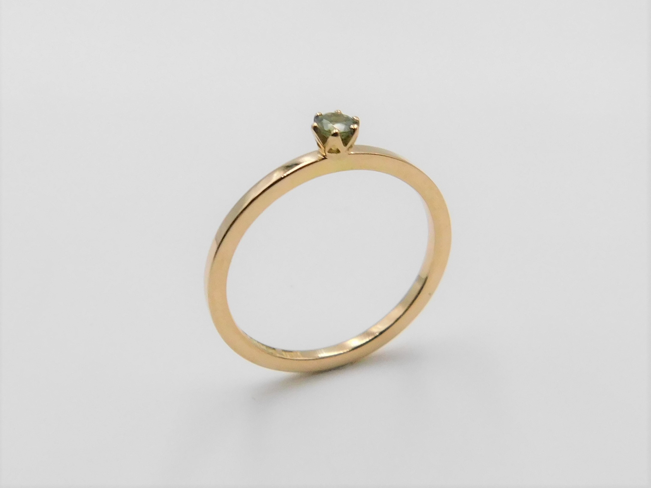 Ring Elly i 18K guld med grön safir stående mot ljus bakgrund
