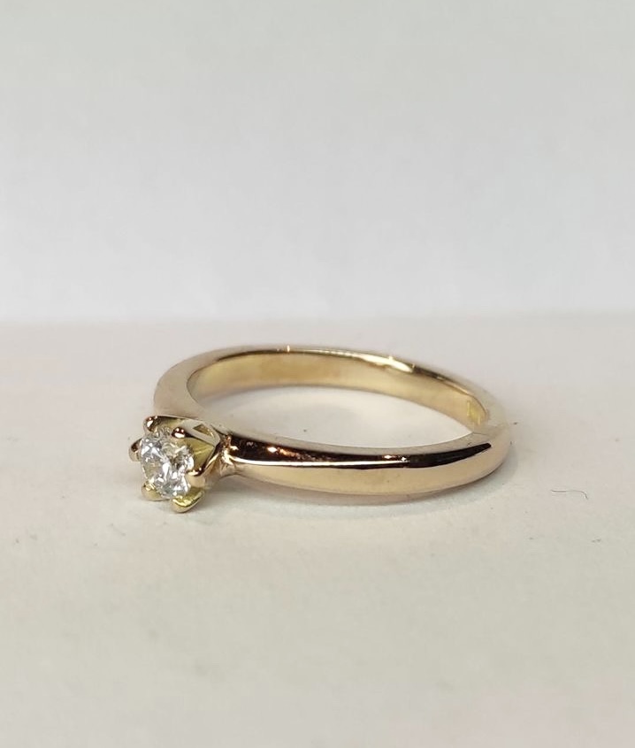 Ring Julia i 18K guld med briljantslipad diamant i centrum liggandes mot ljus yta