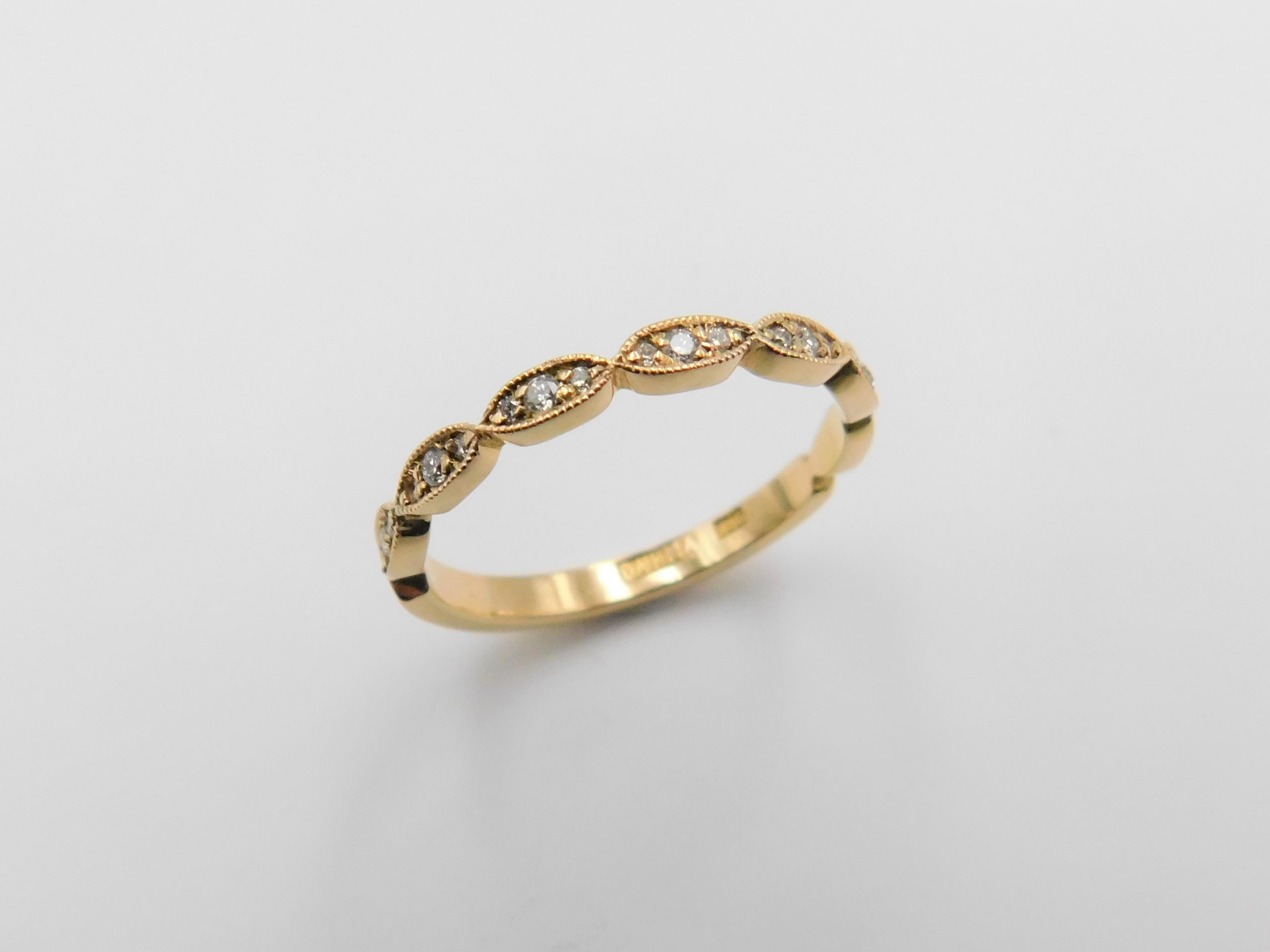 Ring Stina i 18K guld med vågformad profil och briljantslipade diamanter, stående mot underlag