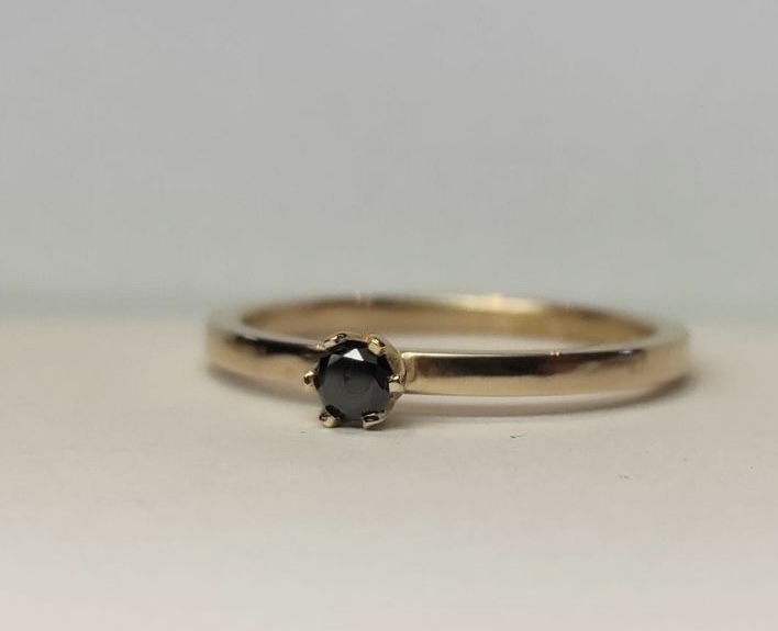Ring Elly i 18K guld med svart diamant liggande på ljust underlag
