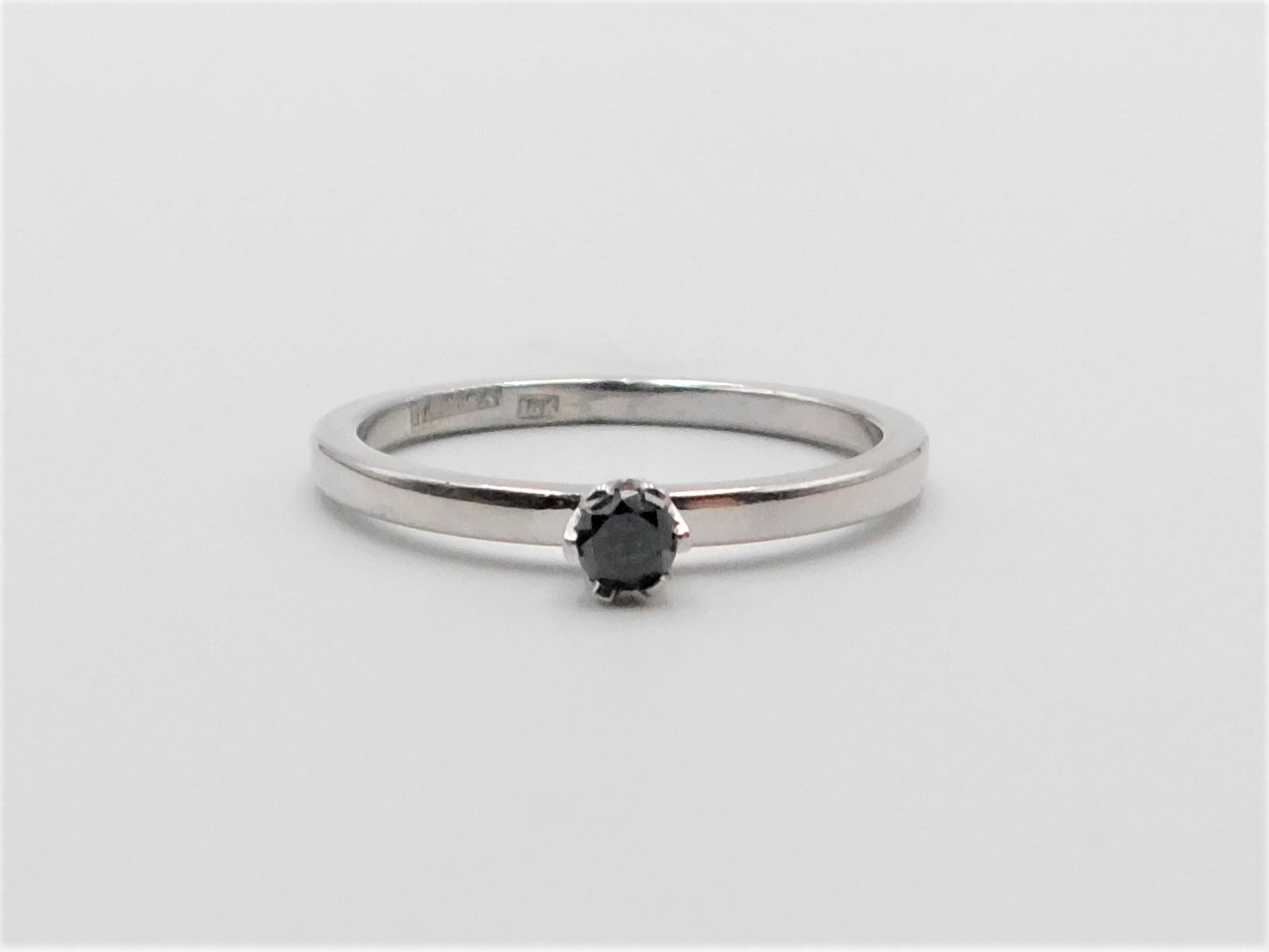 Ring Elly i vitguld med svart diamant liggande på ljust underlag