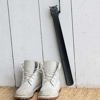 Metal Shoehorn Owl, black decorative shoehorn in the shape of an owl, made of powder-coated steel, hanging from a wall next to a pair of shoes