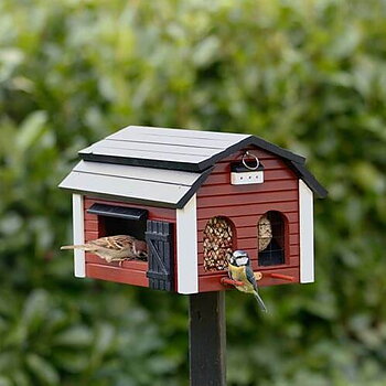 Multiholk Barn Red, bird feeder painted with environmentally friendly colours, in a garden setting with a bluetit and a tree sparrow on it