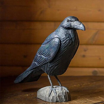 DecoBird Raven, hand carved wooden bird painted with environmentally friendly colours, in front of a wooden wall