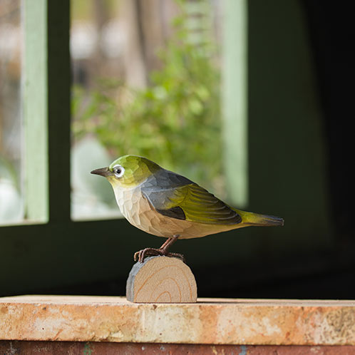 DecoBird Silvereye, hand carved wooden bird painted with environmentally friendly colours, in front of a window