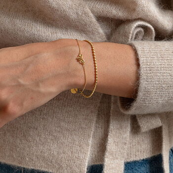 Syster P Lunetta armband guld, enkelt kedjearmband med små ovala länkar, stylat tillsammans med ett tunnare guldarmband mot beige stickad tröja.