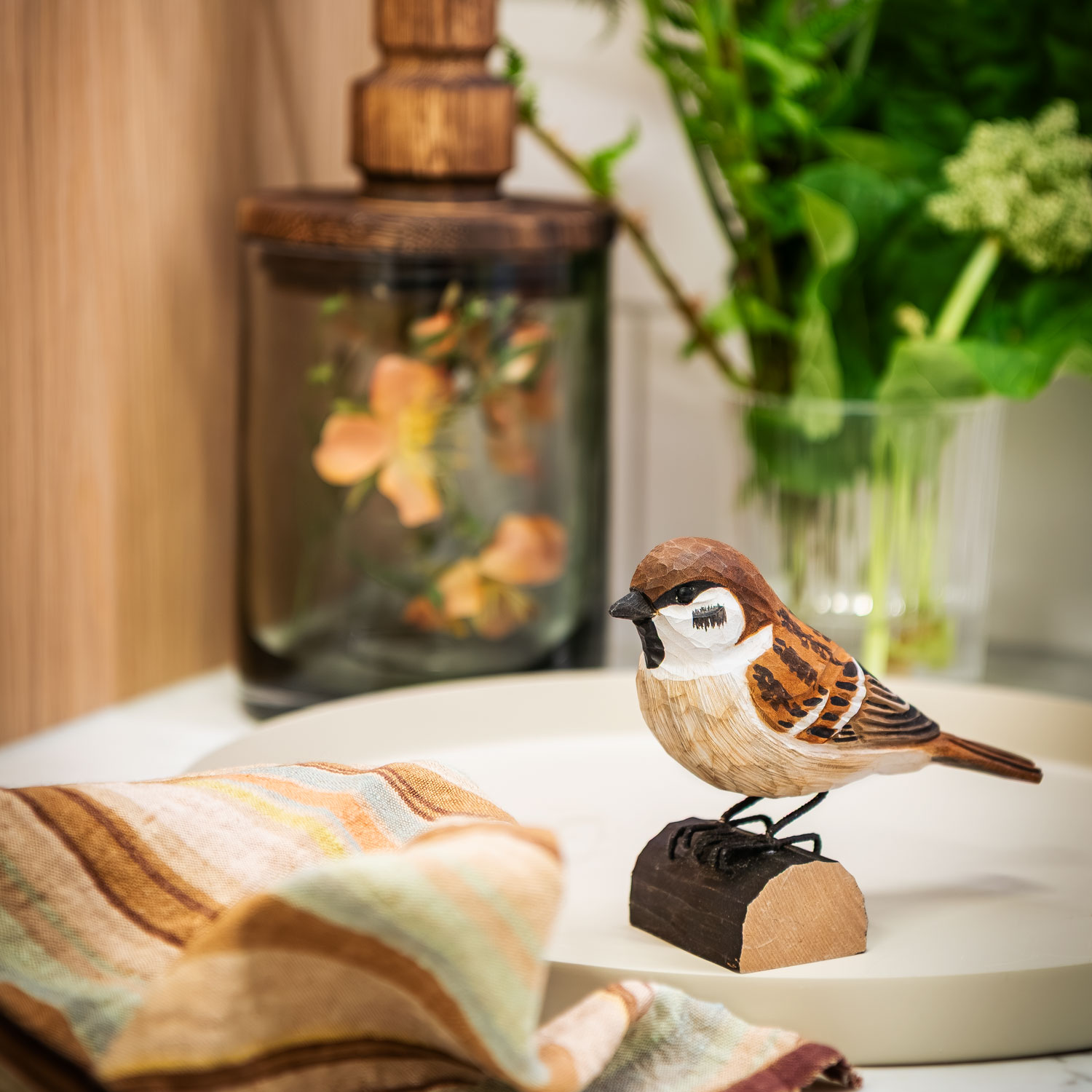 DecoBird Tree Sparrow placed on a tray beside a striped napkin and green plants.