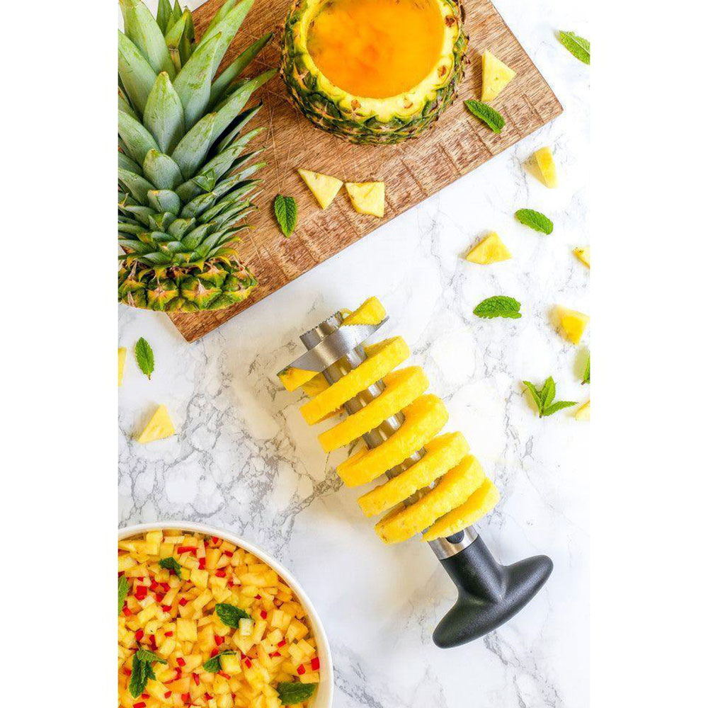 Ananasskärare med spiral av ananas och hackad ananas på köksbänk