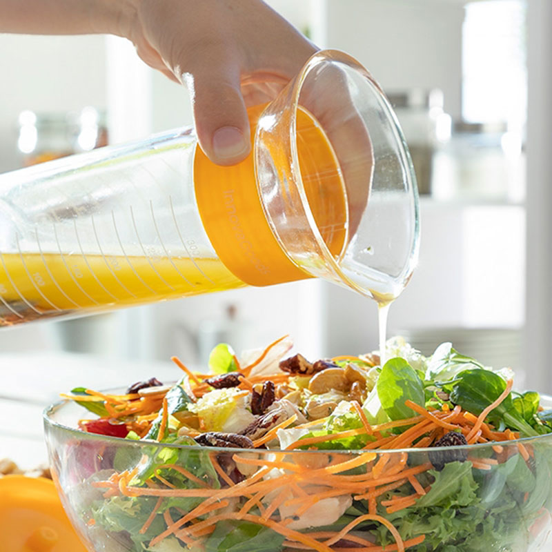Dressingsflaskan med blandning häller dressing på sallad