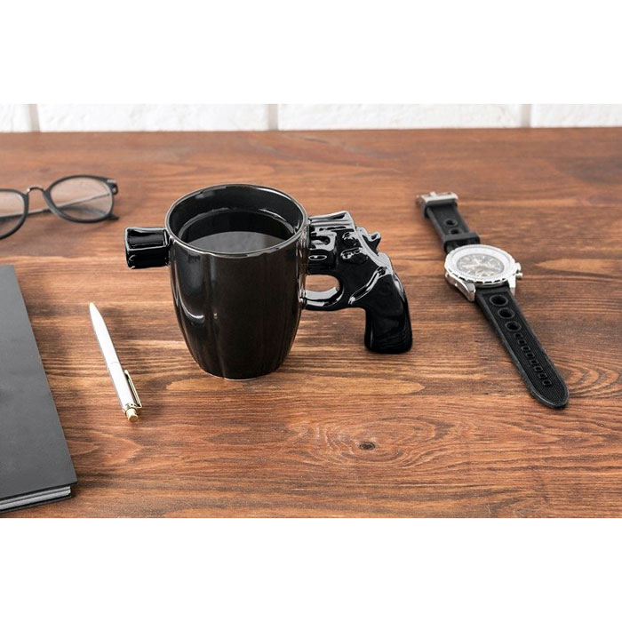 Svart pistol-mugg med kaffe på skrivbord