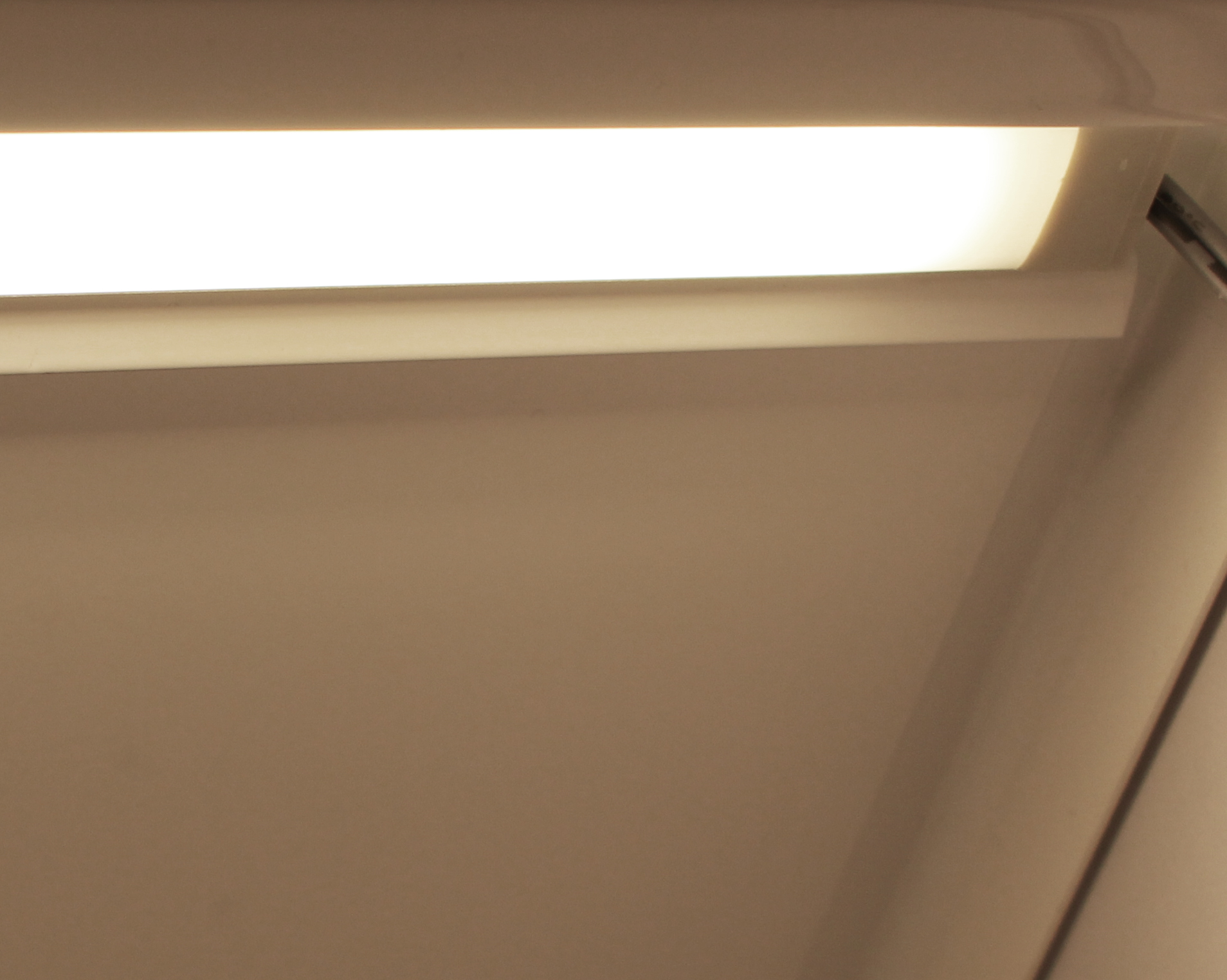 Maggie Hyldebelysning 900 – slank LED-lysskinne monteret under en hylde, som giver ensartet belysning af bøger; magnetmontering for nem installation.