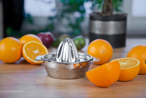 Teräksinen sitruspuristin ja appelsiinit