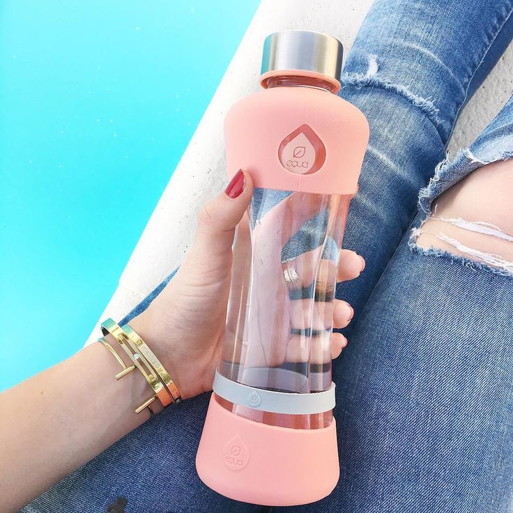 Hand håller i vattenflaska av glas med rosa hölje