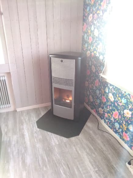 Pelletskamin Lilla Frö svart med grå front. Gnistskydd svart metall. Råspont på ena väggen, tapeter på den andra.