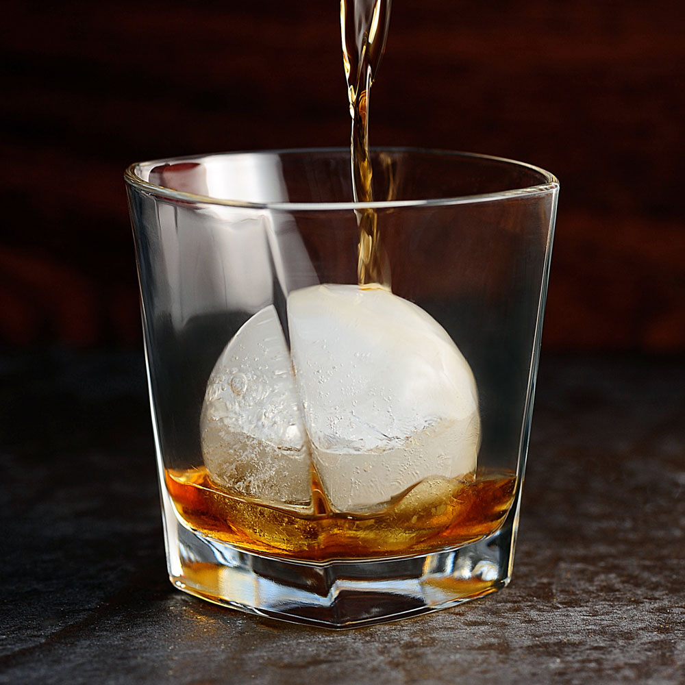 Isklot i ett glas där whisky hälls över isklotet