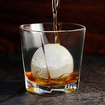 Isklot i ett glas där whisky hälls över isklotet