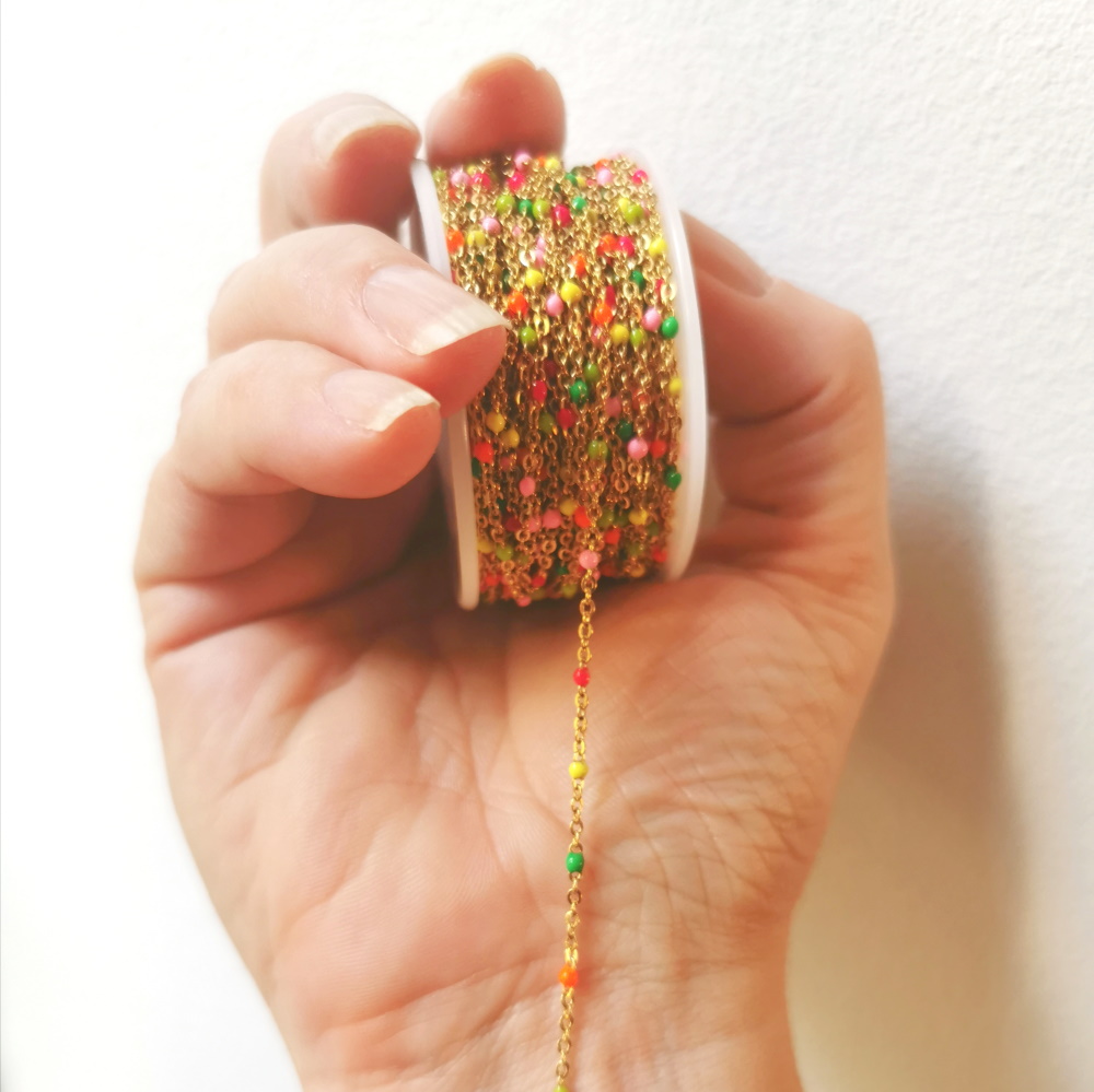 Candy-kedja i guldfärgat rostfritt stål med små emaljkulor, tunn ankarkedja med kulor ca 2 mm, visad i hand.