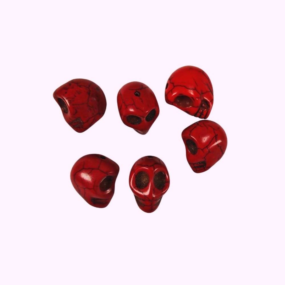 Röda dödskallepärlor i pressad howlit, cirka 17×18 mm med hål på 1,5 mm, visade i närbild mot rosa bakgrund.