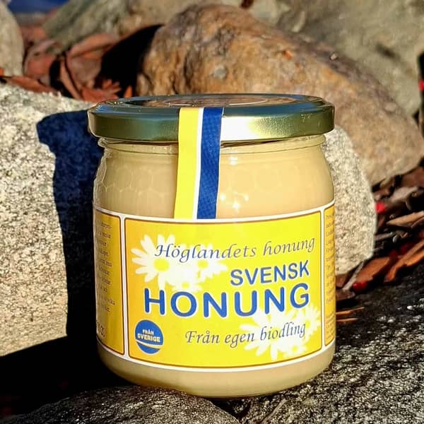 Glasburk med svensk honung och officiellt sigill på rustik stengrund. Höglandets honung 500 gram.