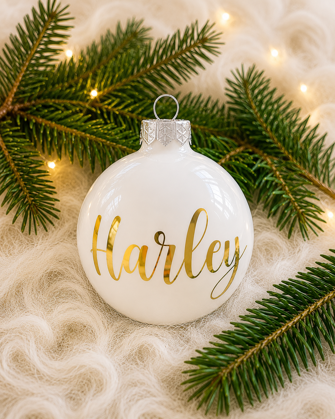 Personlig vit julkula i glas med namnet Harley i guldfärgad text, omgiven av granris