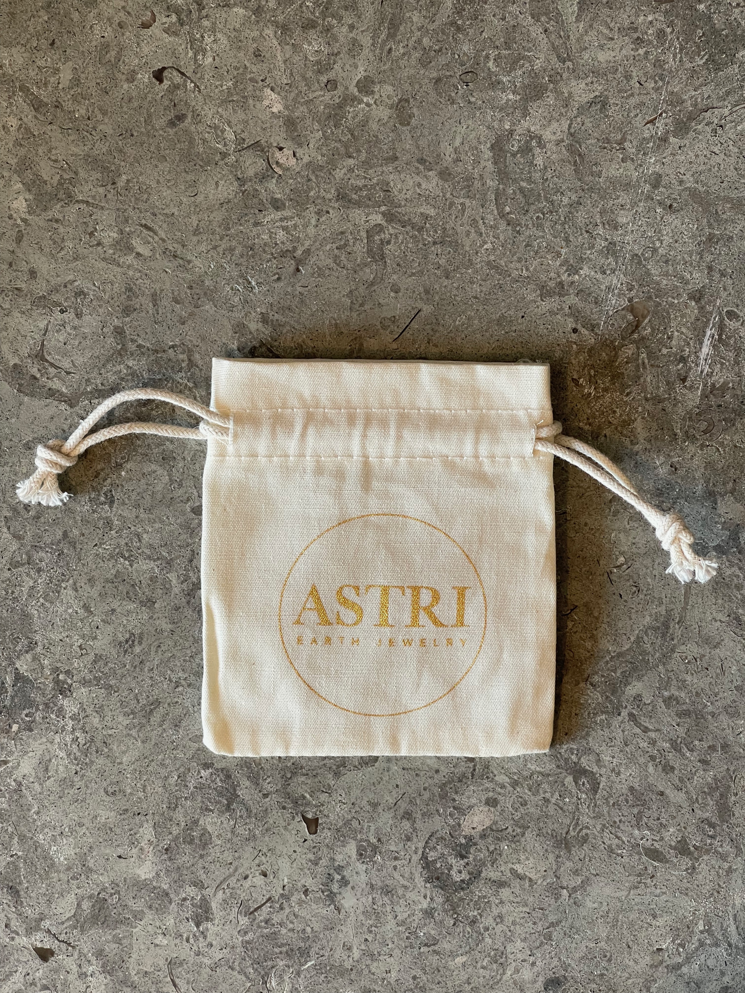 Tygpåse i en beige, varm nyans med Astri Jewelry's logga i guld. 