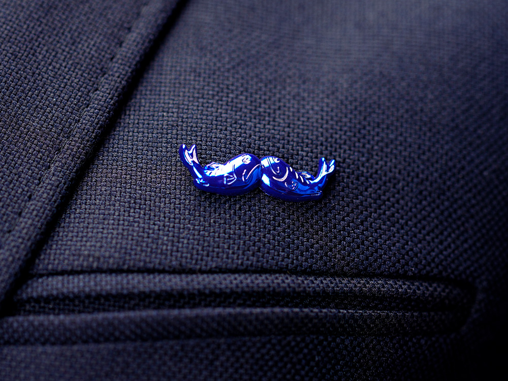Två blå fiskar formade som en mustasch-pin fästa på en mörk kavaj