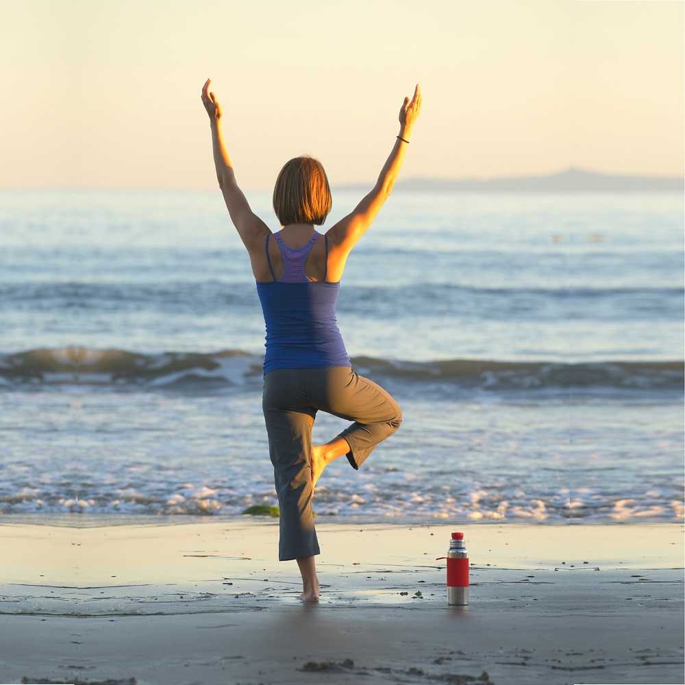 Person gör yoga på strand med vattenflaska bredvid