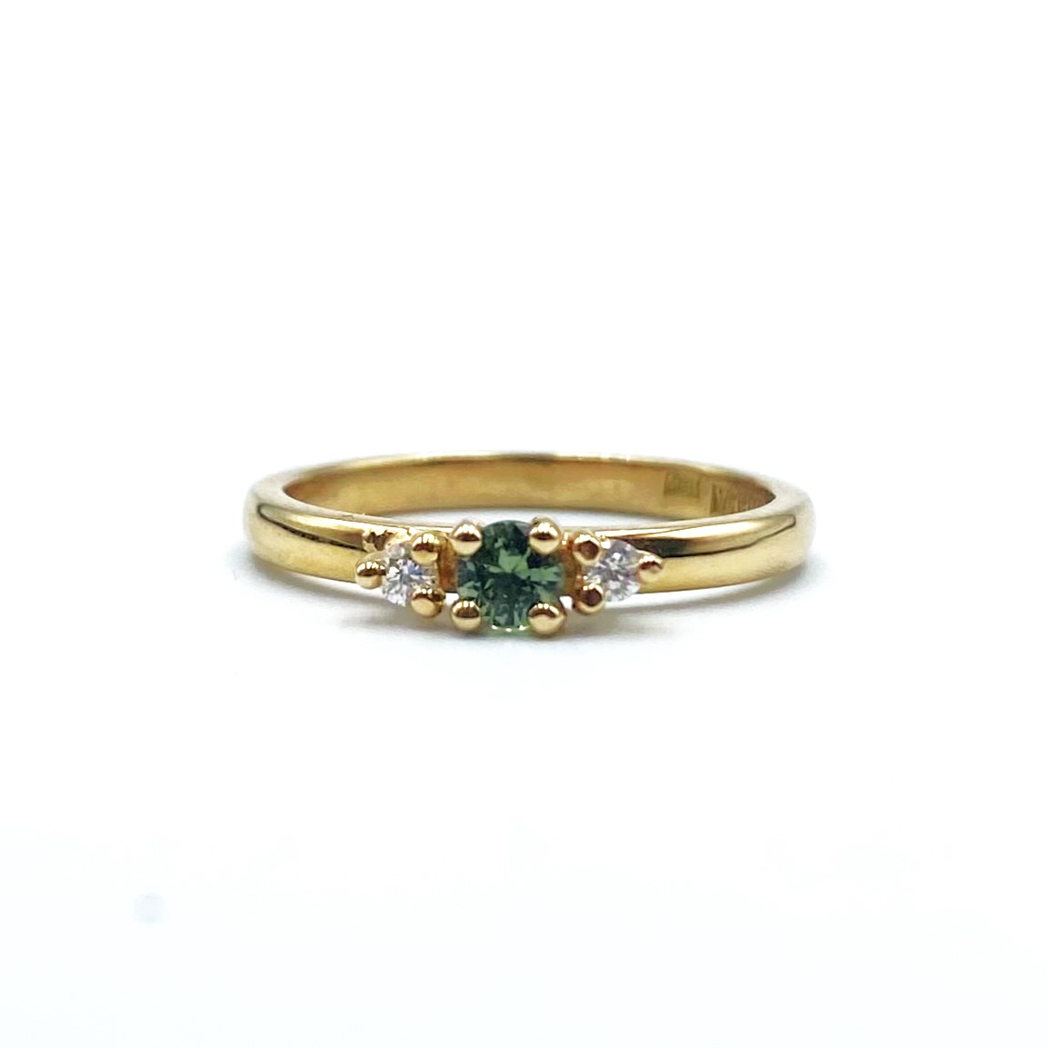 Ring Louise i 18K guld med grön safir och briljantslipade diamanter liggande mot vit bakgrund