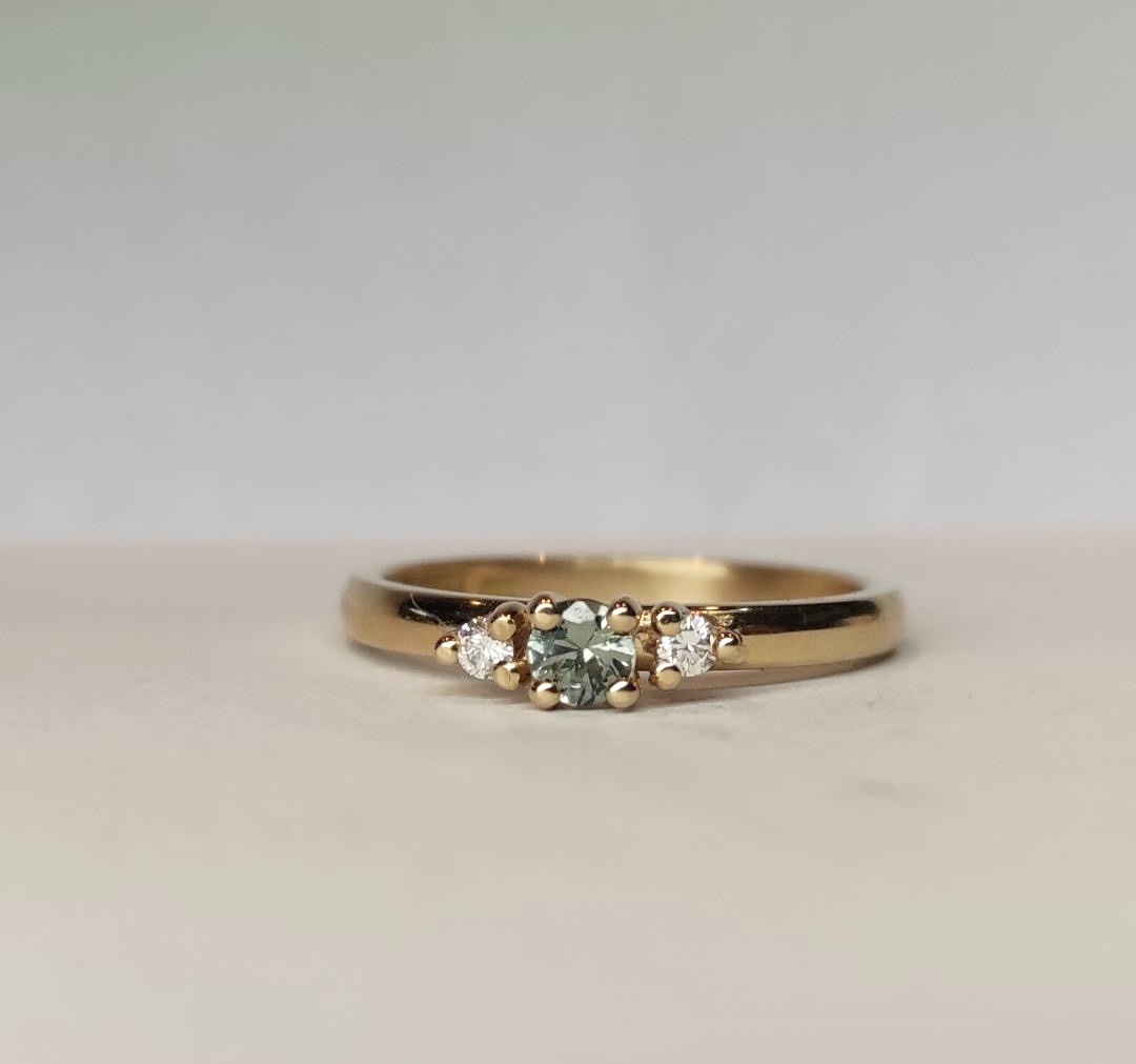 Ring Louise i 18K guld med grön safir och briljantslipade diamanter liggande mot underlag