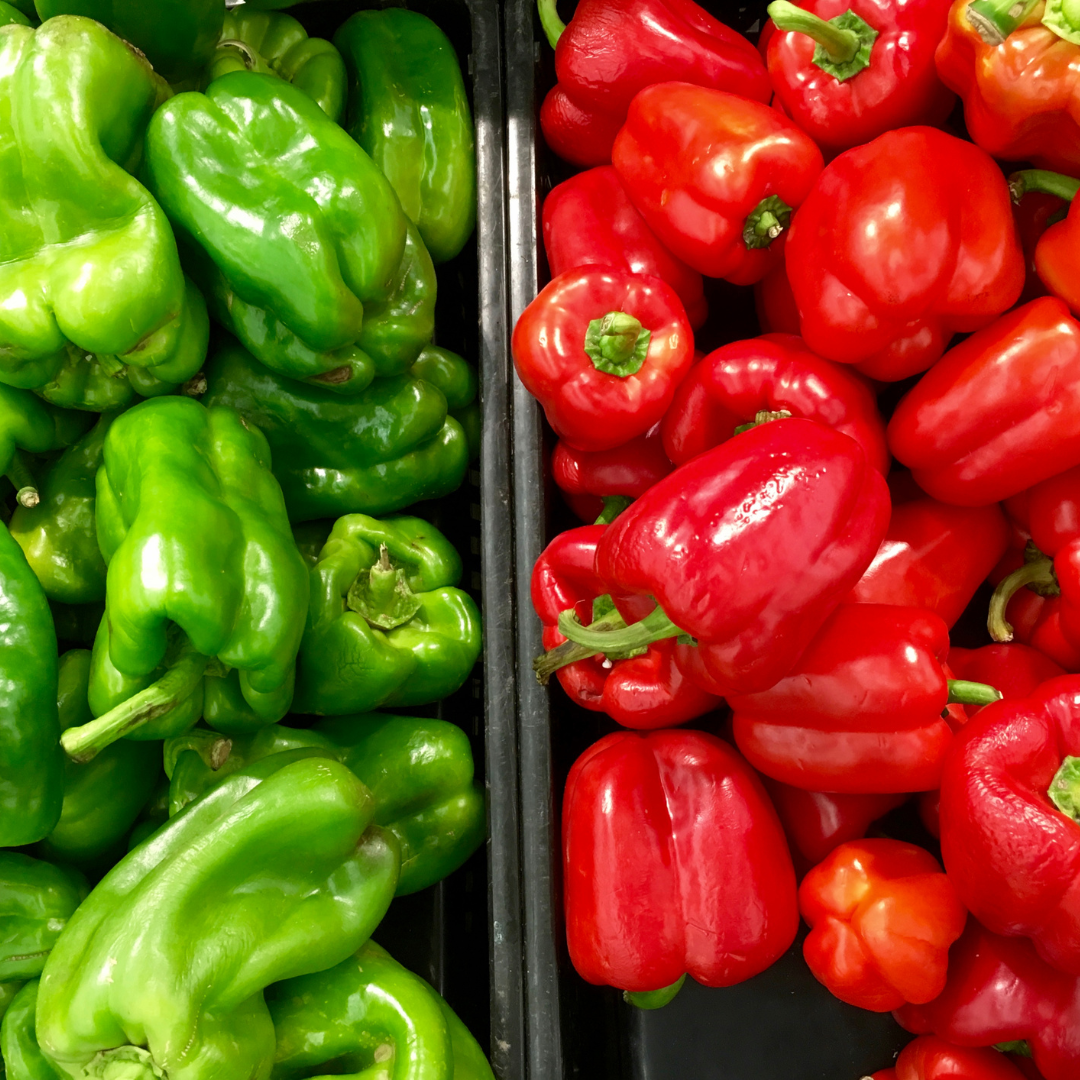 En närbild av gröna samt  mogna röda paprikor av sorten 'Dulce de España'. Frukterna är stora, köttiga och något avlånga med en lätt spetsig form. De har en glänsande, djup röd färg. Paprikornas yta är jämn och inbjudande, och de ser både saftiga och smakrika ut.