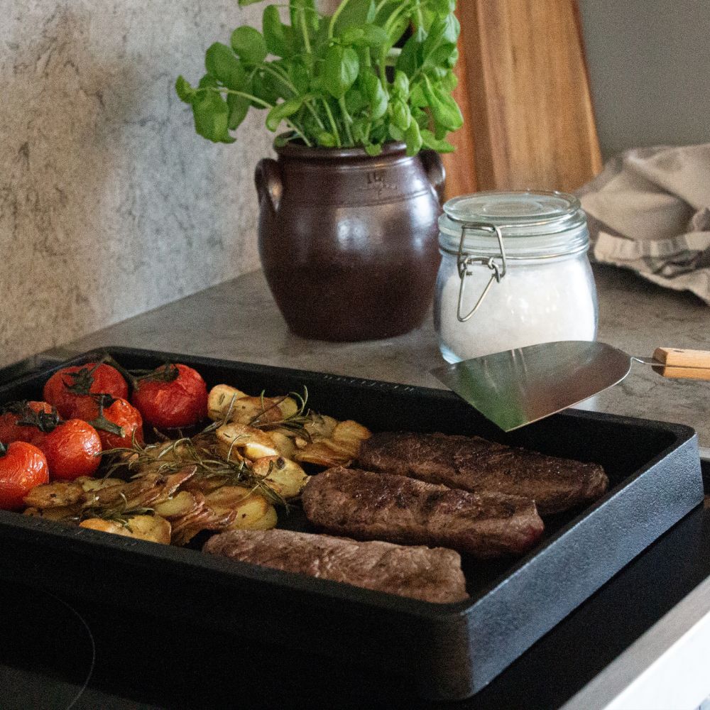 Bøffer, kartofler og tomater tilberedes på et stegebord Queen i støbejern.