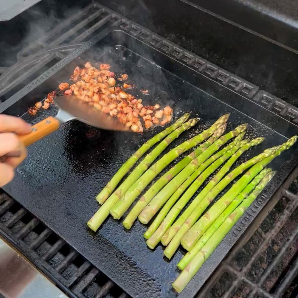 Grønne asparges og bacon tilberedes på et stegebord Original på en gasgrill.