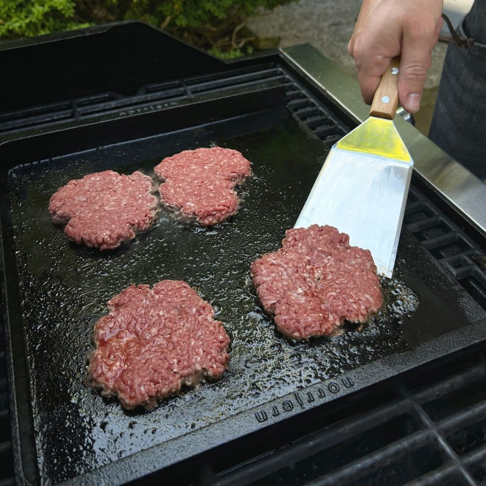 Fire burgere steges på et stegebord Original i støbejern på en grill.
