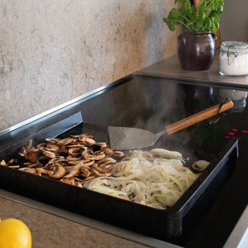 Stegte svampe og løg på et stegebord Original placeret på en kogeplade.
