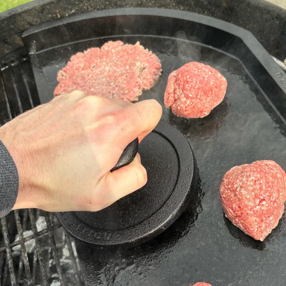 Kød presses ud til flade burgere ved hjælp af en hamburgerpresse. Stegebordet passer perfekt i en Weber kuglegrill.