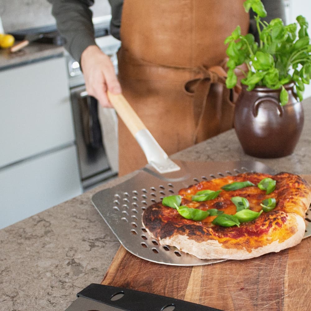 Pizzaspade fra norrjern bruges til at tage bagt pizza ud, pizzaen toppes med basilikum