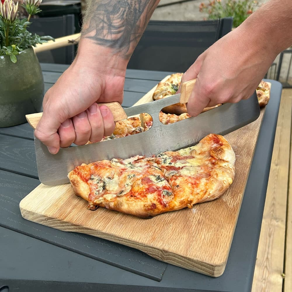 Pizzaskærer fra norrjern bruges med to hænder og skærer en pizza op