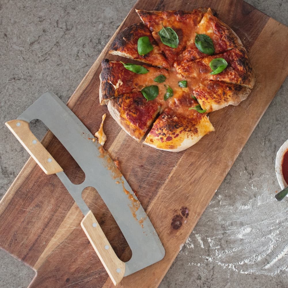 Pizzaskærer og pizza fotograferet ovenfra sammen med et træbræt