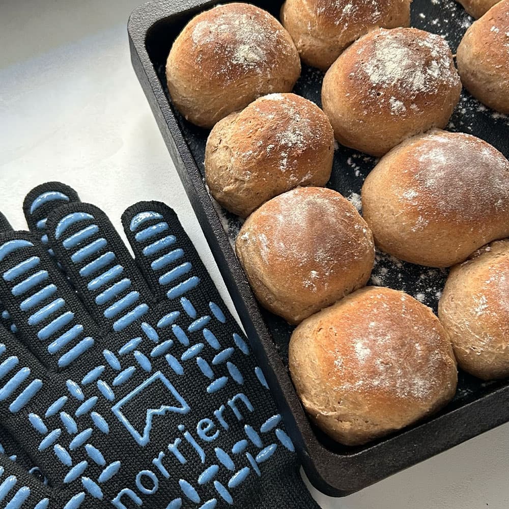 Nærbillede af materiale og syninger på en grillhandske Pro samt stegebord og nybagt brød