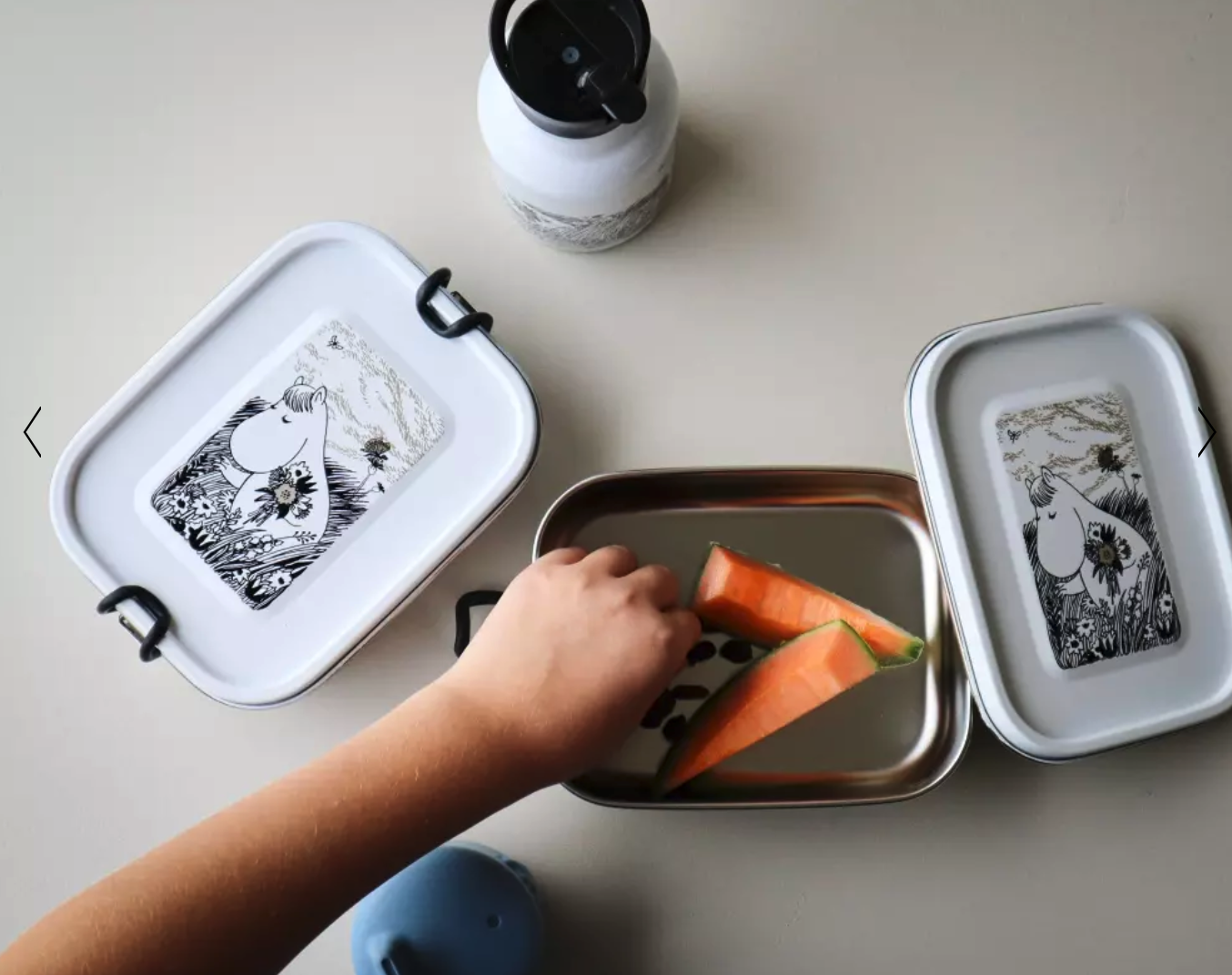 Käsi ottaa ruokaa valkoisesta teräksestä Muumikuvalla varustetusta lounaslaatikosta