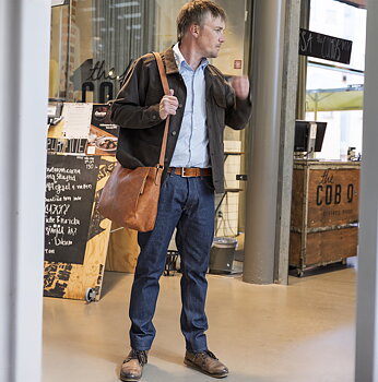 stående man med brun overshirt,ljusblå skjorta naturfärgat bälte och matchande axelväska i skinn bärande slim 100% bomull i mörkblå rawdenim