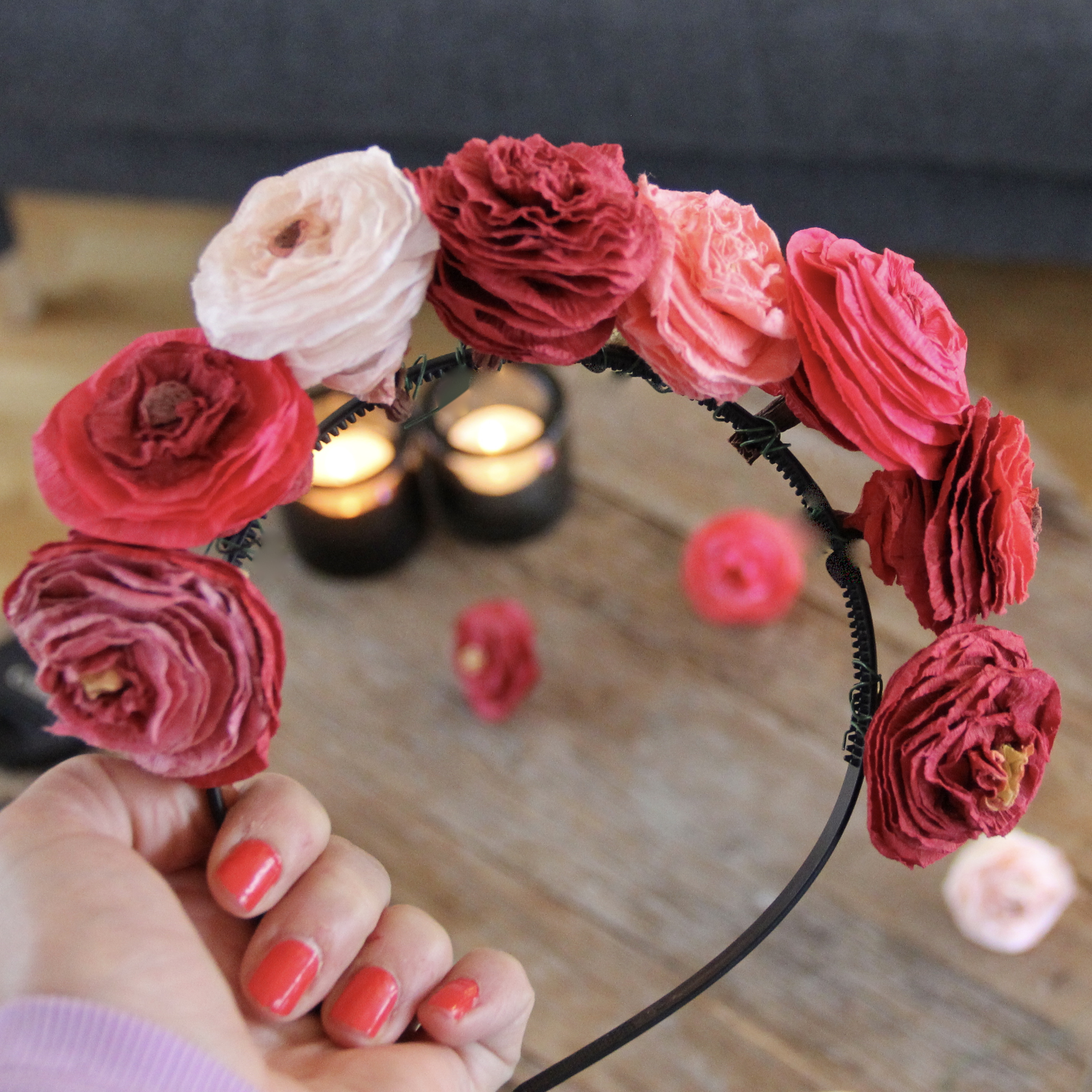 Hand som håller i ett blomsterdiadem med rosor i olika rosa färger.