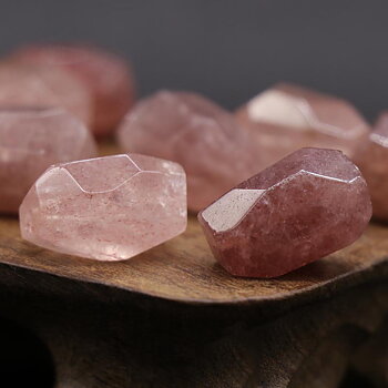 Facetterade bumlingar av jordgubbskvarts, rosa stenar med glansig yta och naturliga inneslutningar, visade i närbild på ett träfat.