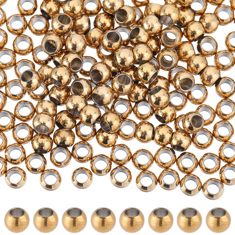 Närbild på små runda förgyllda stålpärlor, ca 4 mm stora, med slät glansig yta och stort hål, arrangerade i grupp på ljus bakgrund.