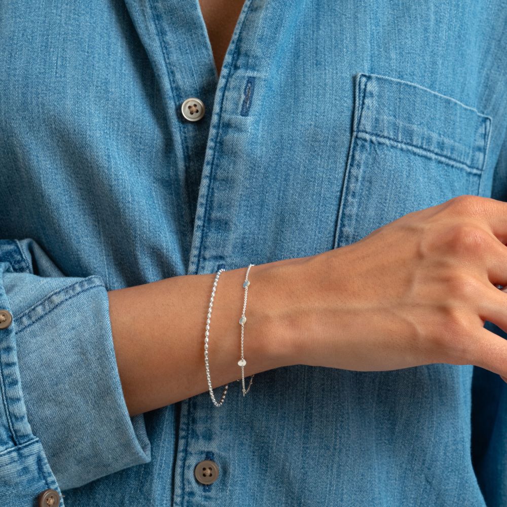 Syster P Lunetta armband silver, tunt armband med små ovala kulor i sterling­silver, stylat tillsammans med Syster P Solea armband mot denimskjorta.