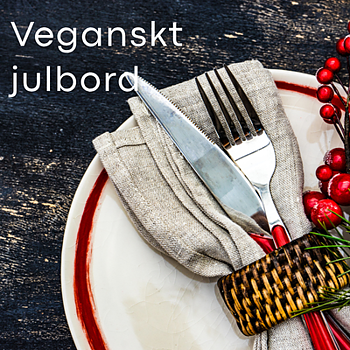 Festligt dukat julbord med vegansk tema – vit tallrik med röd kant, bestick i naturfärgad servett, röda bär och rustik träbakgrund.